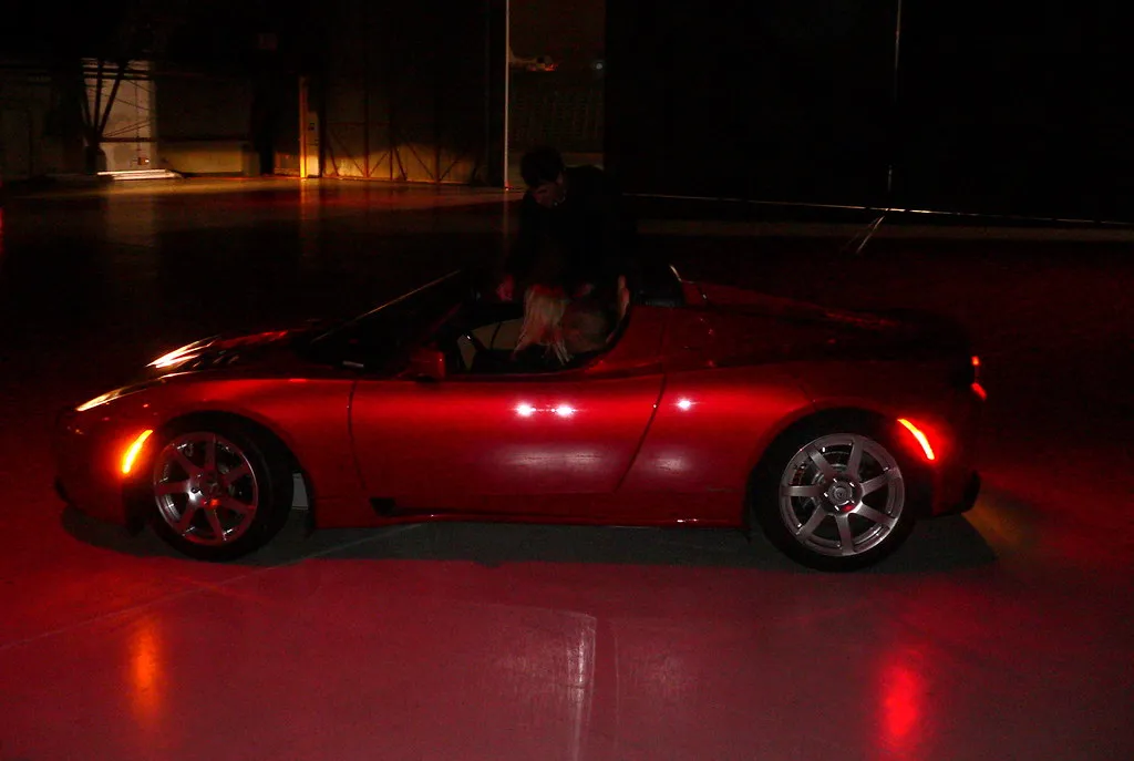 A red Tesla Roadster parked in a dark studio